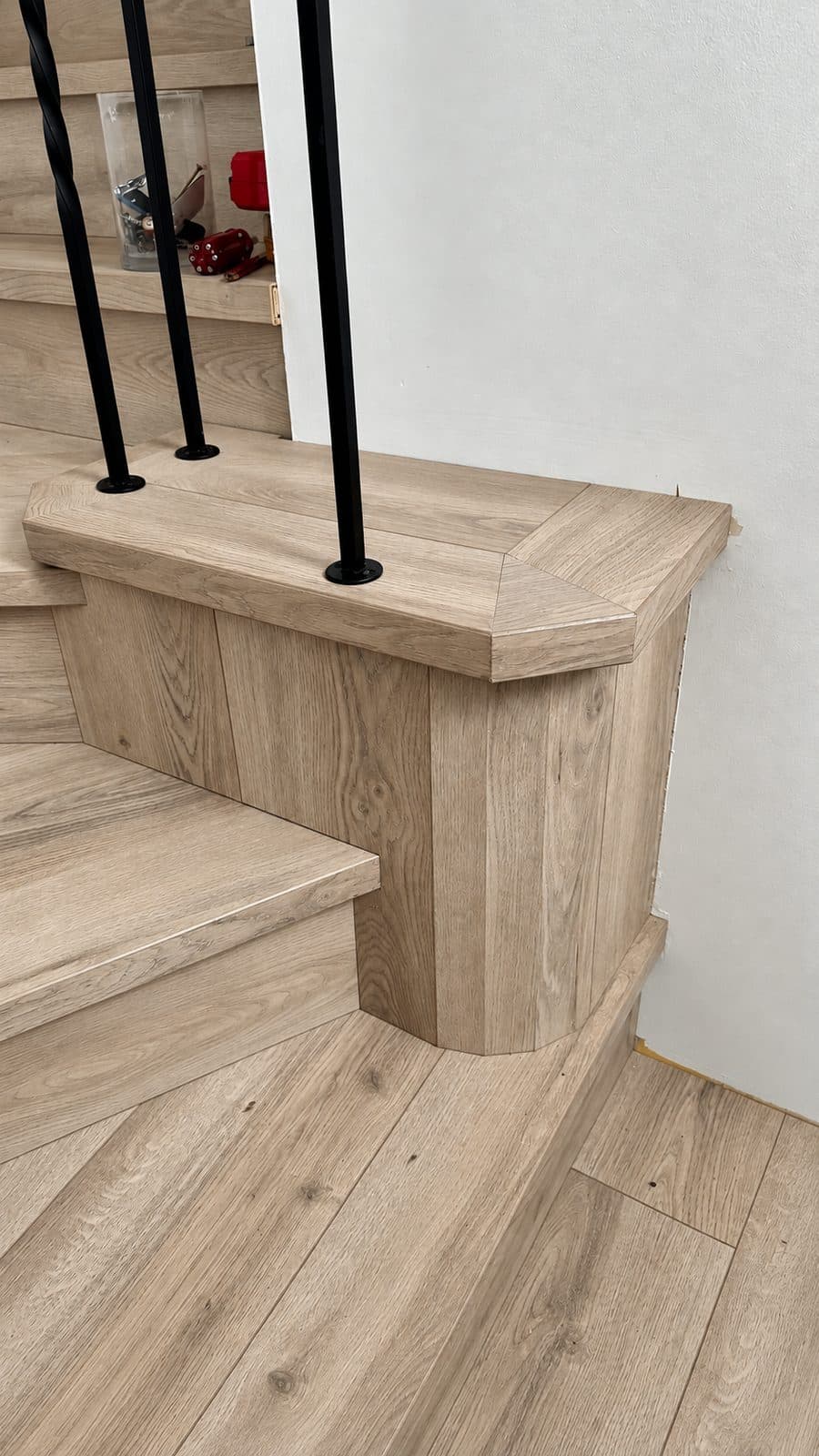 Stair landing with a wood-clad newel base beside black balusters