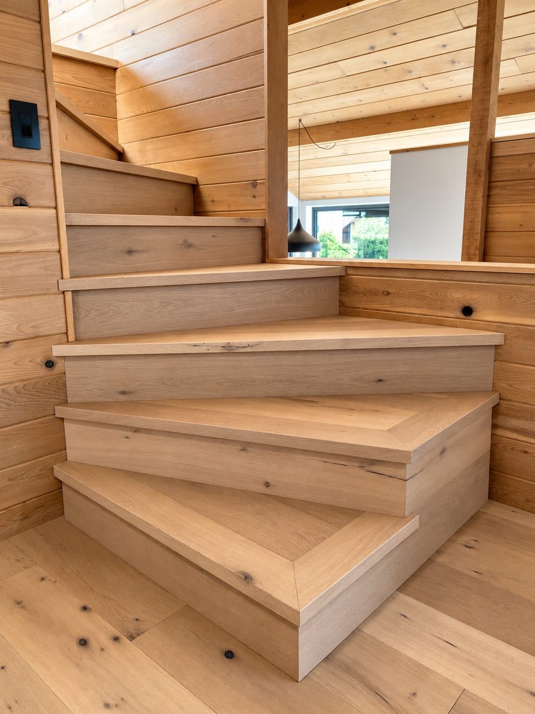 Winding staircase with light wood treads against cedar walls