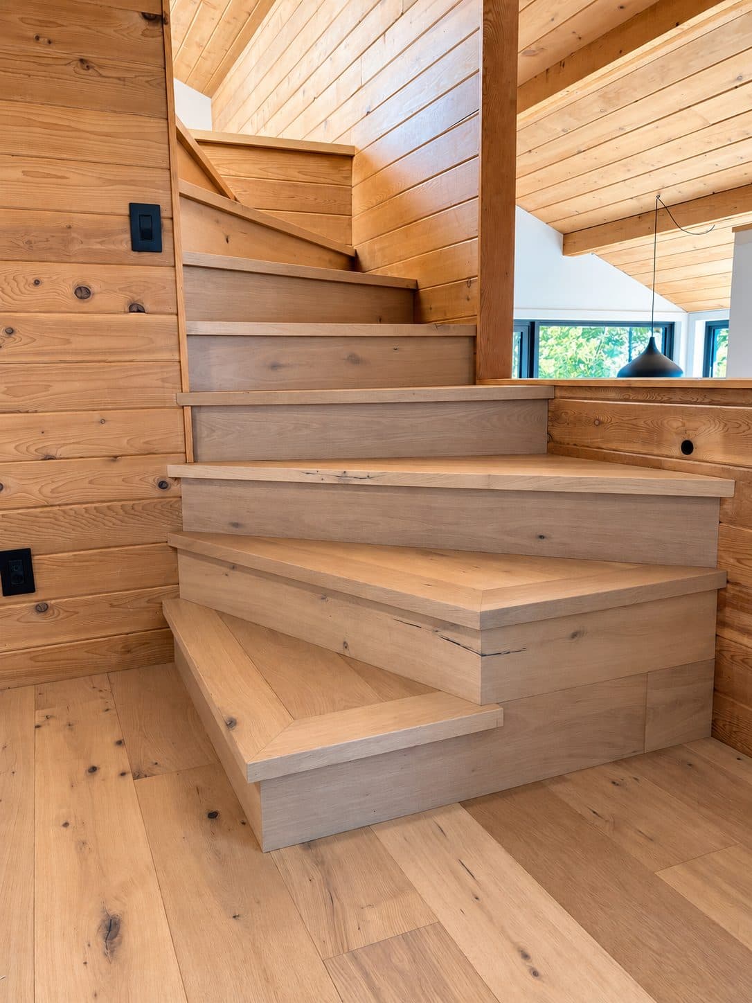 Winding staircase with light wood treads and square nosings beside cedar walls
