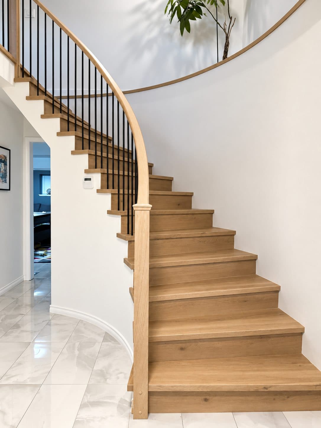Curved wood staircase rising from a marble foyer