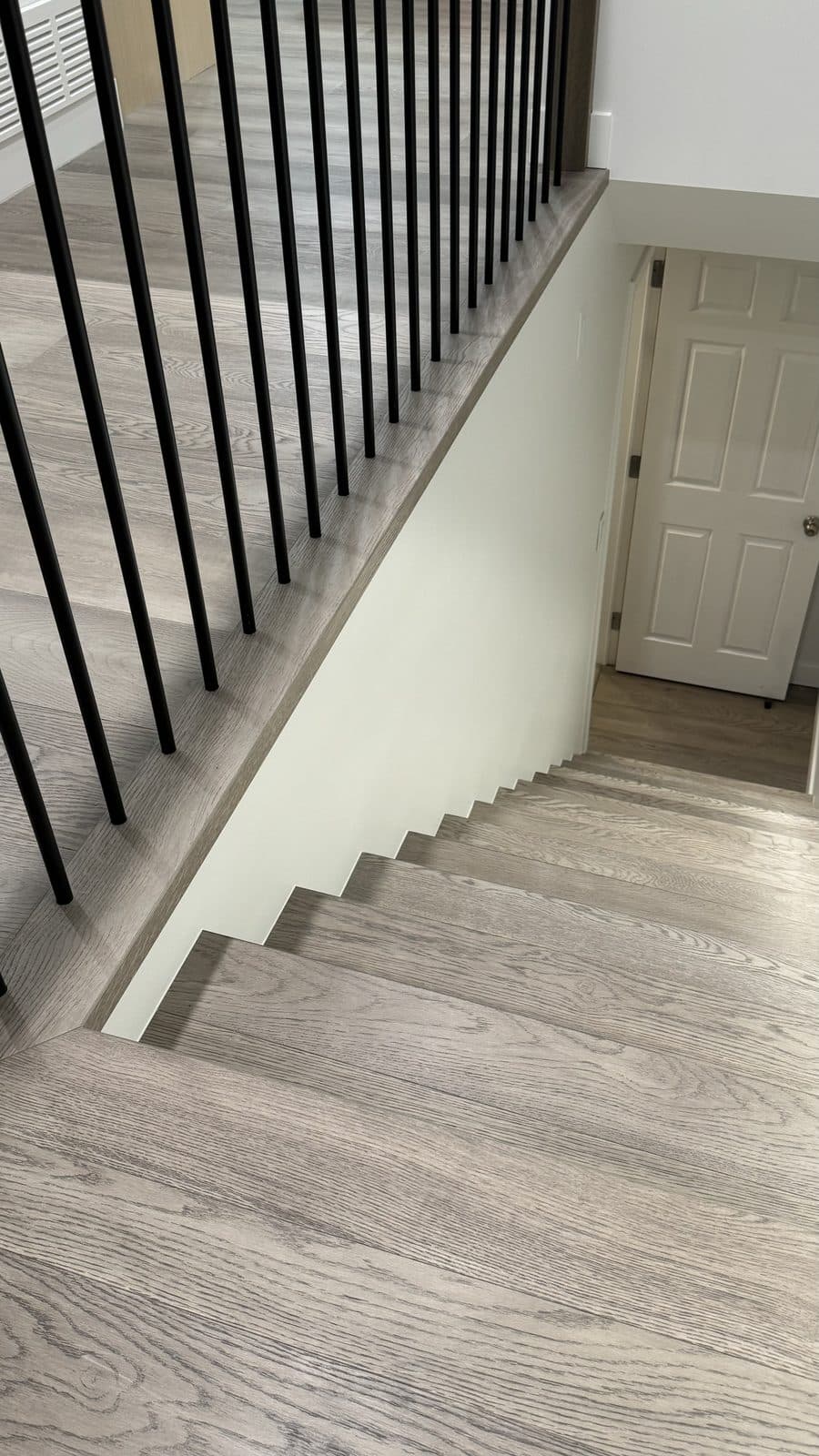 Grey wood stairs turning beside black balusters